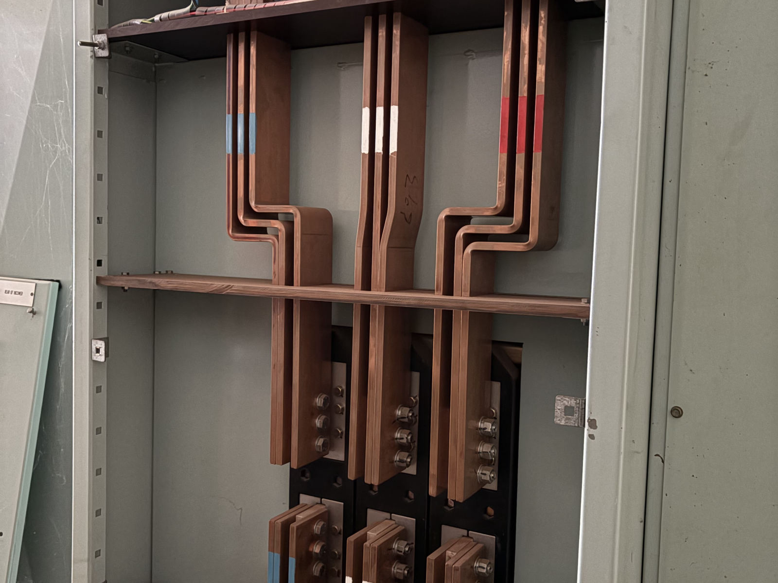 Copper busbar chamber inside a switchboard showing bolted connections and phase-coloured marking